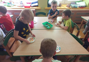 Dzieci przy stolikach przyklejają kuleczki w plasteliny.